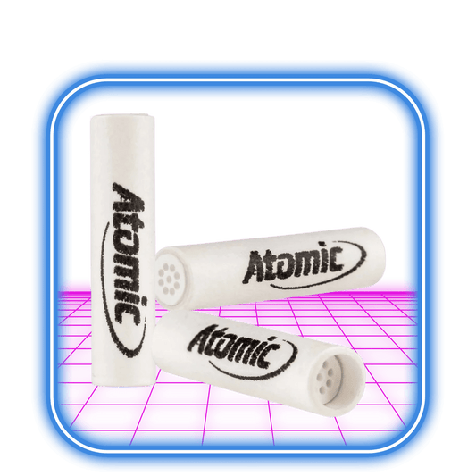 Tre vita cylindriska AT-filter | 6 mm Active Charcoal (10-pack) från Atomic, med den svarta Atomic-logotypen, är arrangerade på en rosa och lila bakgrund med en blå kant. Varje filter har små hål för att göra röken mindre skadlig och mer smakrik.