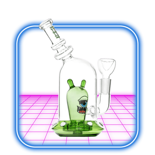 HEMPER Space Monster Bong 7'' - Green har en nyckfull enögd utomjording med ett busigt leende, tillverkad av borosilikatglas och mot en livfull rosa och blå digital bakgrund i en rundad fyrkantig ram.