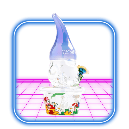 En 10,7'' Hemper Trippy Gnome XL Bong, formad som en tomte och märkt HEMPER, sitter på en genomskinlig låda med färgglada blommor och svampar mot en levande rosa och blå digital bakgrund.
