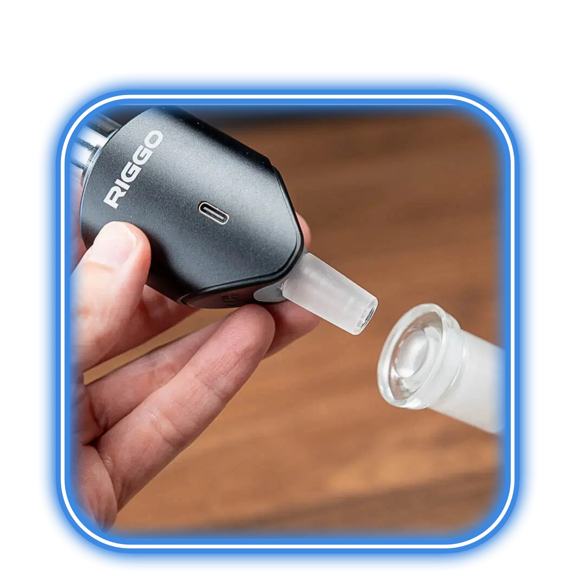 En hand håller XMAX | Riggo - Svart vaporizer från XMAX nära en glasadapter, med en träyta bakom. Scenen ramas in av en blå rundad kant.